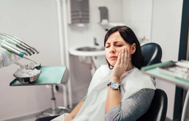 Woman in dental chair holding her cheek in pain