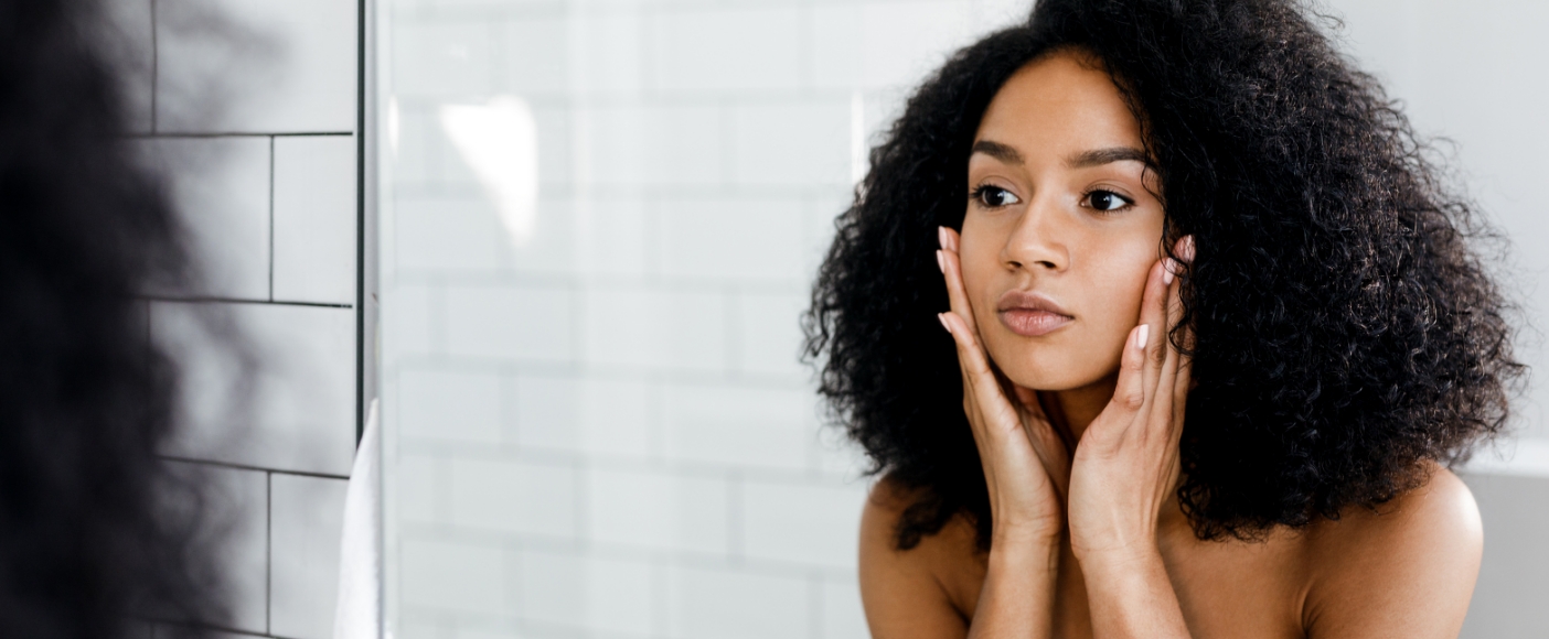 Young woman touching her face while looking in mirror