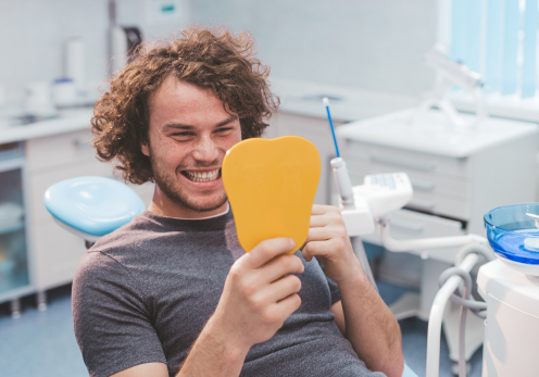 Young man in dental chair admiring his smile in yellow mirror