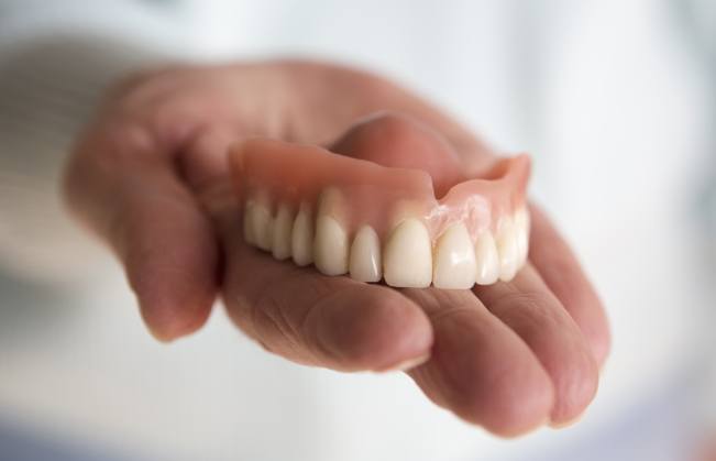 Person holding a full upper denture in their hand