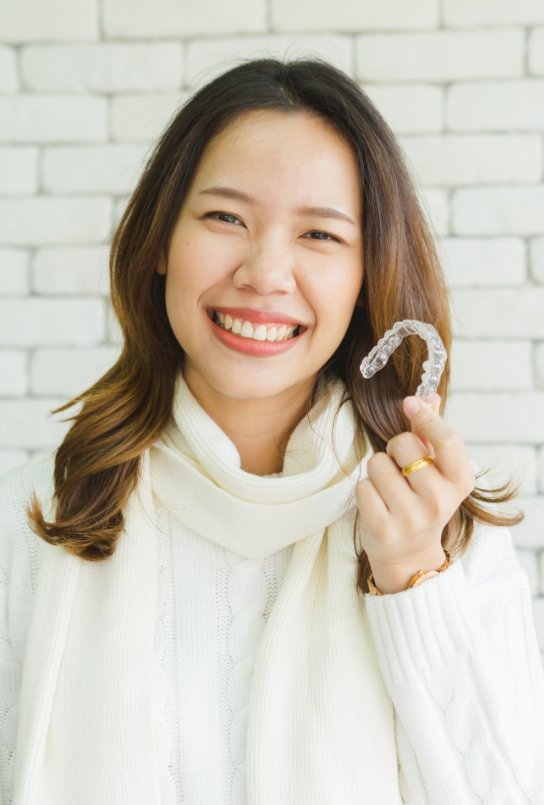 Smiling woman holding SureSmile clear aligner in Covington