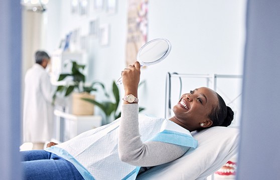 Woman looking at smile in handheld mirror at dentist's office