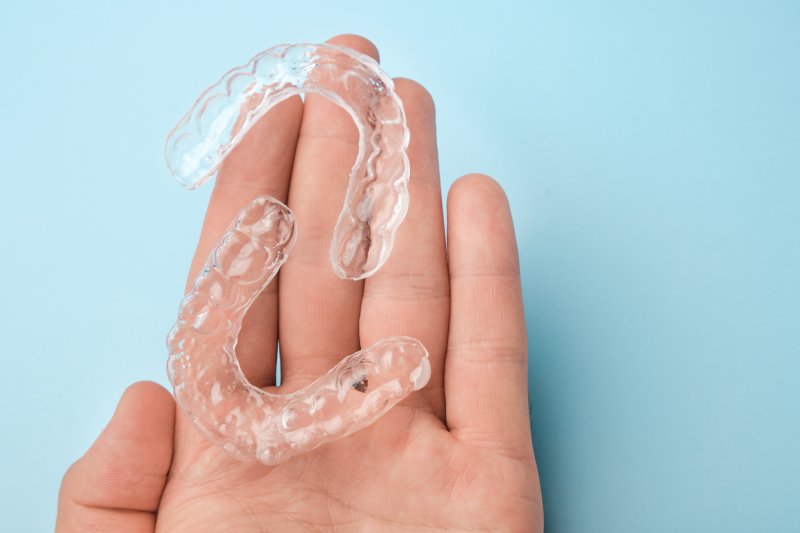 A close-up of a hand holding two clear aligners